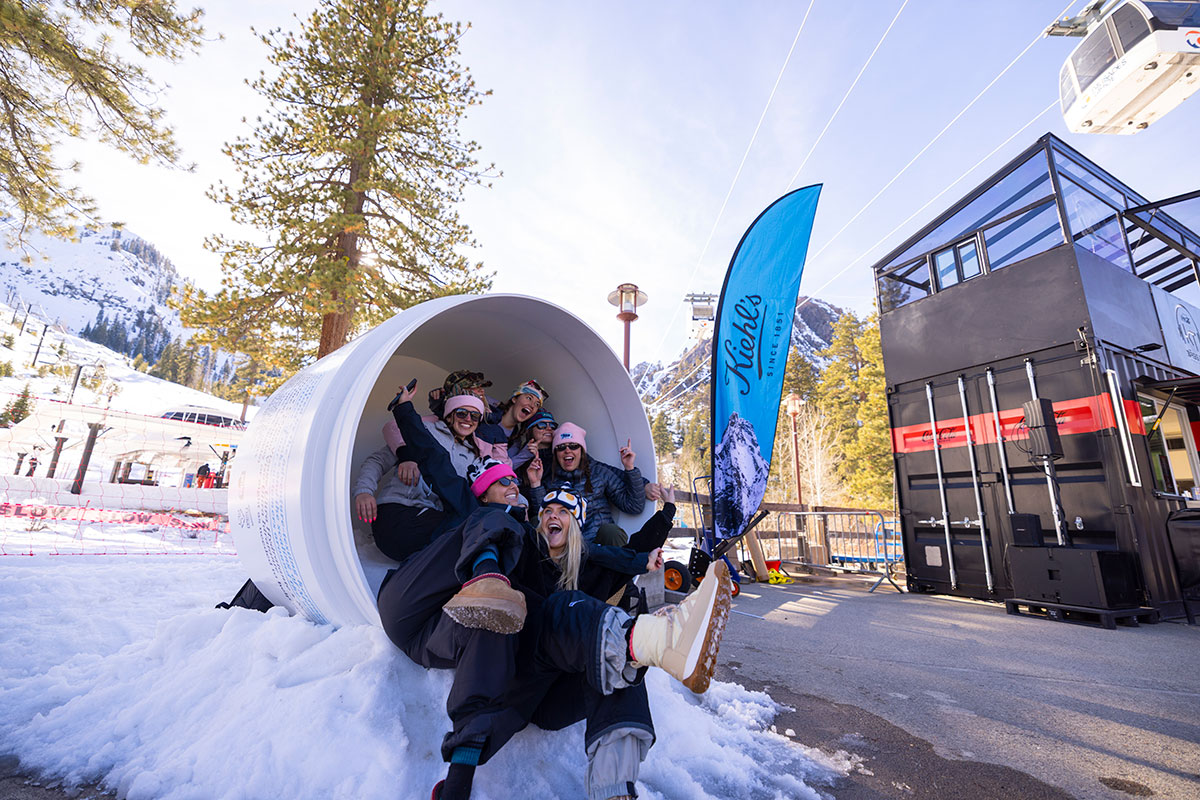 Group of friends laughing inside a Kiehl's branded ski-through tube at a mountain resort